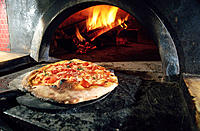 Pizza emerges from a wood buruning oven in Naples. Italy
