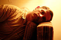 man lying on couch with head on arm of couch, eyes open, stark orange interior lighting
