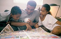 African-American father and children reading newspaper´s comics
