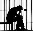 Sitting man. head in hand, silhouetted against jail bars.