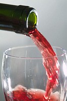 Someone from a green bottle pouring red wine into a wine glass