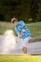 Boy, age 14, hitting out of sandtrap on golf course. McCall, Idaho USA