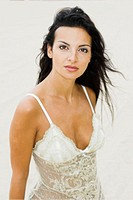 A young 20´s, 30´s woman wearing a lace white top, looks into camera with a pleased and sexy expression with her long black hair blowing in a breeze