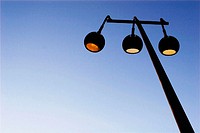 Three street lamps on pole at dusk against a clear blue sky.