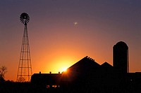 Sun rising over farm buildings with a windmill
