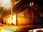 A warehouse on a desolute street corner is captured at night with a slight blur creating a mysterious, painterly effect.