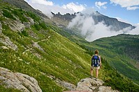 Female hiker pausing on rock outcrop to take in view of the Garden Wall as seen from the Highline Trail in Glacier National Park, Montana, USA