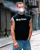 A young man smoking in the downtown streets of Manhattan. He is smoking Marlboro Reds and his tattoos are of pin-up girls. His shirt says ´bow down´.