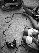 Brothers and sisters sit on the rug playing video games. Some anxiously await the turn at the remote. All watch the TV.