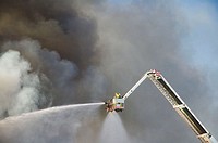 Firefighter in crane sprays water on fire through clouds of black smoke. Perth, Western Australia.