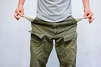 Young man pulling his pockets out to illustrate lack of money.