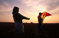 children flying a kite together outdoors at sunset