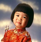 Young Asian girl in traditional embroidered top with Cheerios on chopsticks.