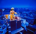 High angle view of two firemen in a high-reach apparatus, overlooking a city at dusk