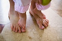 Close-up of mother and infant girl´s barefeet. Infant is standing on mother´s feet.