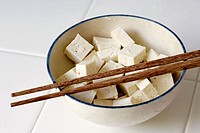 Pieces of Tofu cut into cubes and sitting in a bowl with a pair of chopsticks resting on top.