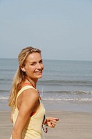 Beautiful blonde woman wearing headphones and smiling on a beach in India.