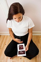 Pregnant woman looking at her unborn child on print of her ultrasound scan.