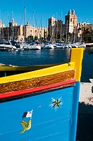 La imagen muestra en primer término la popa de un luzzu, un barco de pesca típico maltés. Al fondo, se puede ver el frente marítimo de Vittoriossa, do...