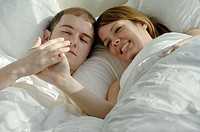 Young adult couple together in bed looking at hands