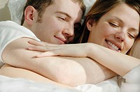 Young couple cuddling together in bed smiling