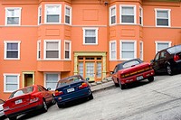 Cars parked in front of a bright, well_maintained orange house on a very steeply sloped section of Jones Street in San Francisco, California. The stre...