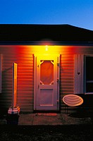 Illuminated roadside motel room entrance door and porch with chair at dawn
