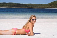 Woman lying on white beach, smiling at camera. Fraser Island, Australia