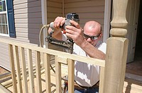 Construction worker building new home deck railing with wood and with nailgun and saw