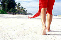 Woman walking along the beach at Unguja Island while only her legs are visible and a part her red skirt, Zanzibar Archipelago, Tanzania, East Africa.