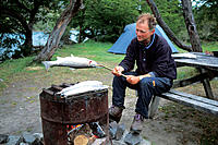 Man barbecueing a salmon trout, Torres del Paine National Park, Patagonia, Chile