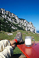 Feet of a hiker with hiking shoes next to a glass with fresh milk, Mount Kampenwand, Chiemgau, Upper Bavaria, Germany
