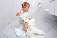 Llittle girl sitting on Potty in bathroom, unrolling toilette paper while doing potty training, playing and fooling around