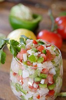 Close-up of large glass filled with Ceviche. Lemon, pepper & tomatoes in background.