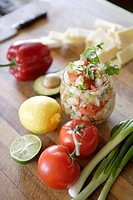 Glass of ceviche, tomatoes, lemon, scallions & lime in foreground, sliced cheese, bell pepper, & avocado in background.