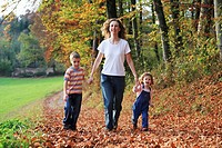 Mother with daughter and son running hand in hand on path full of leaves in fall, having fun and laughing, autumn foliage covering path in forest, aut...