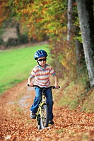 boy riding his bicycle on road with leaves in fall, autumn foliage covering path in forest, autumn, fall, Zuerich, Switzerland