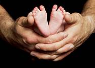 A newborn baby´s feet rest in his father´s hands against a black background.