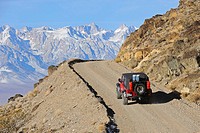 Jeep climbing dirt road with Sierra Mountain Range in background, California, USA
