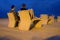 A couple sits on a Barcelona beach at twilight