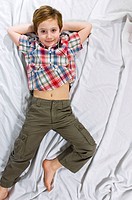smiling baby lying on the bed with his arms behind his head