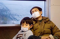 Father and son in train, wearing surgical masks. Japan