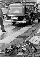 Seventies, black and white photo, traffic, deadly road accident, child had been killed, childs bicycle lies near a cebra crossing, policeman, hearse, ...