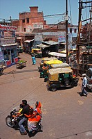 A four-members Indian family on a motorbike, people walking around and some rickshaws parked on a little square in Agra