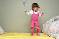 Young girl, two and half years old, bouncing on her bed with a fairy wand.