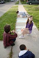 Canada, Ontario, Windsor. Three boys and one girl drawing with chalk on a sidewalk during the summer.
