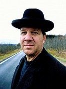 Portrait of a man in a black hat and overcoat standing on a country road.