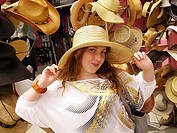 13-year-old girl with long blonde-brown hair and freckles trying on big hat in front of hat display on Venice Boardwalk, Venice, CA