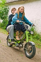 Girl and boy on a moped, girl driving.