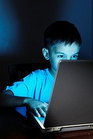 Young Asian boy using laptop at night.